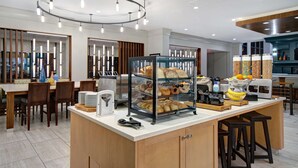 Un bar à petit-déjeuner moderne, doté d’une vitrine réfrigérée où sont exposées des pâtisseries, d  ’une machine à café et d’un panier de fruits.