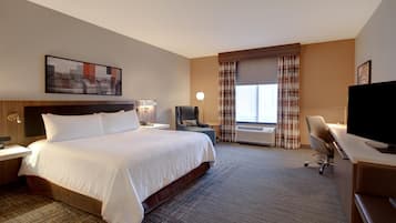 A hotel room with a large bed, a desk with a chair, a television, and a window with curtains.