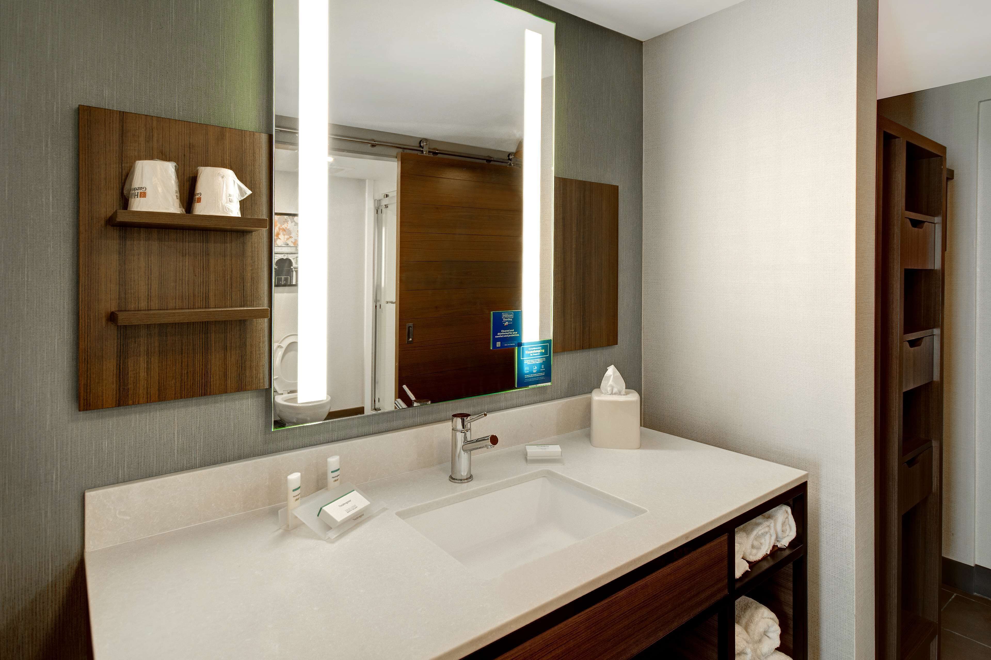Un baño moderno con un espejo grande, un lavabo blanco y estantes de madera.