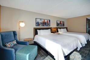 A hotel room with two beds, a blue armchair, a small round table, and two wall-mounted artworks. - Hilton Garden Inn Terre Haute (Terre Haute)