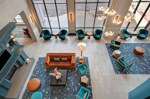 A spacious lobby with a central seating area, multiple green armchairs, and a large window providing natural light.