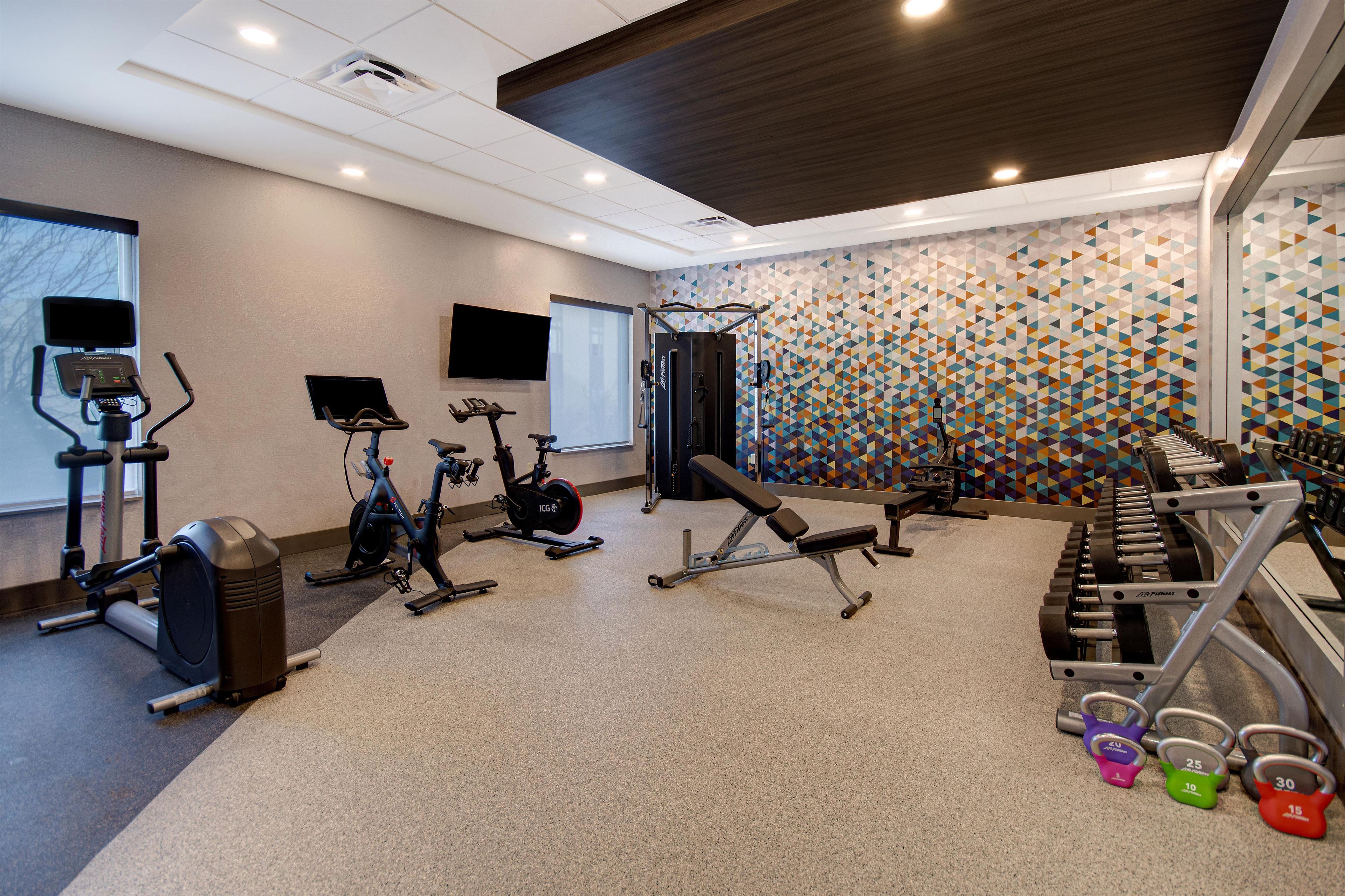 Een fitnessruimte met cardioapparatuur, gewichten en een gestreept wandpaneel.