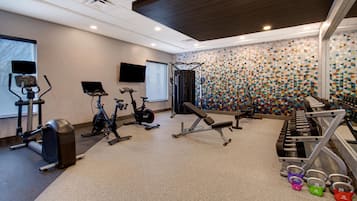 Een fitnessruimte met cardioapparatuur, gewichten en een gestreept wandpaneel.