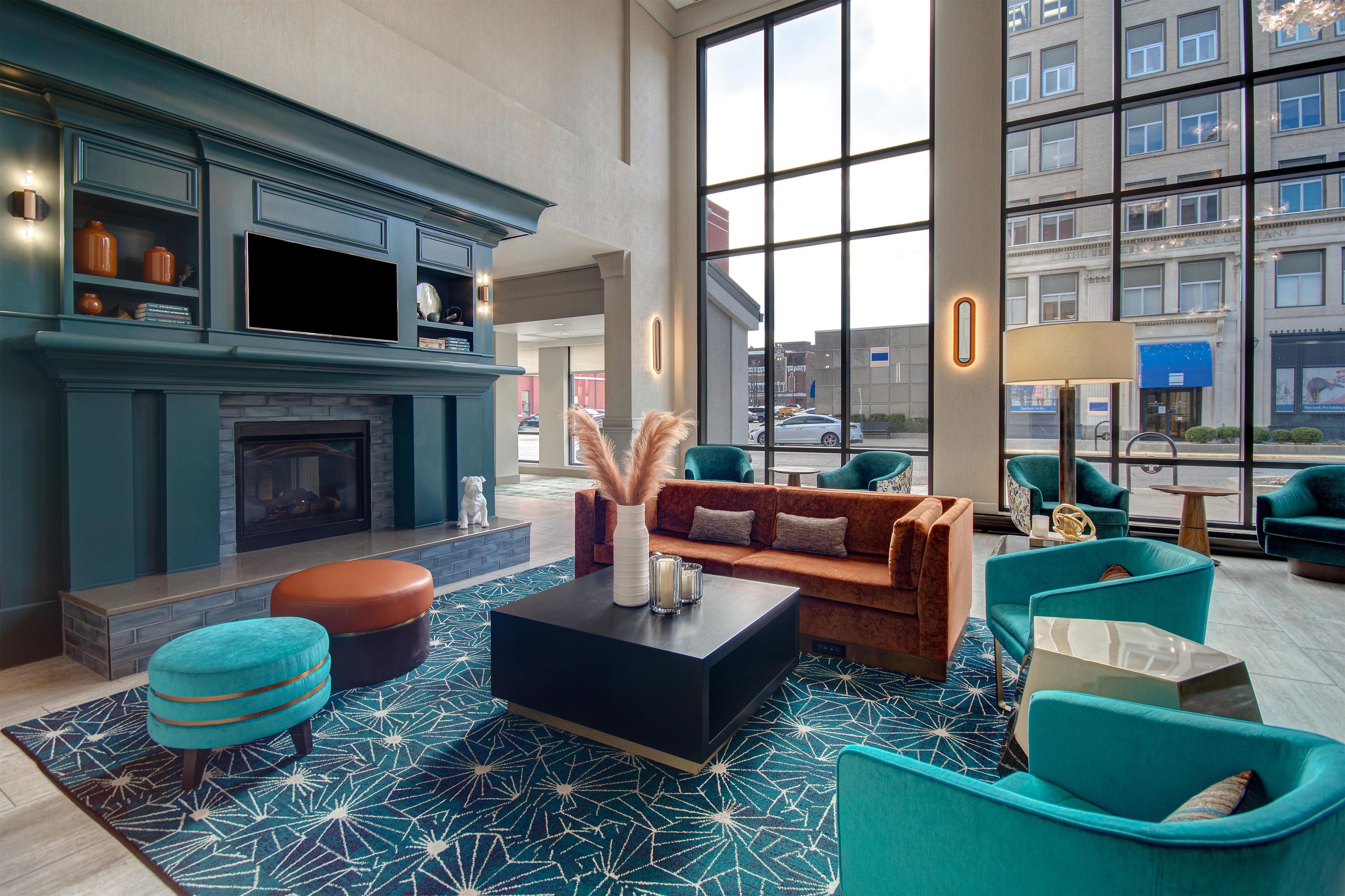 A modern lounge area with a fireplace, comfortable seating, and large windows offering city views.