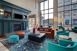 A modern lounge area with a fireplace, comfortable seating, and large windows offering city views. - Hilton Garden Inn Terre Haute (Terre Haute)