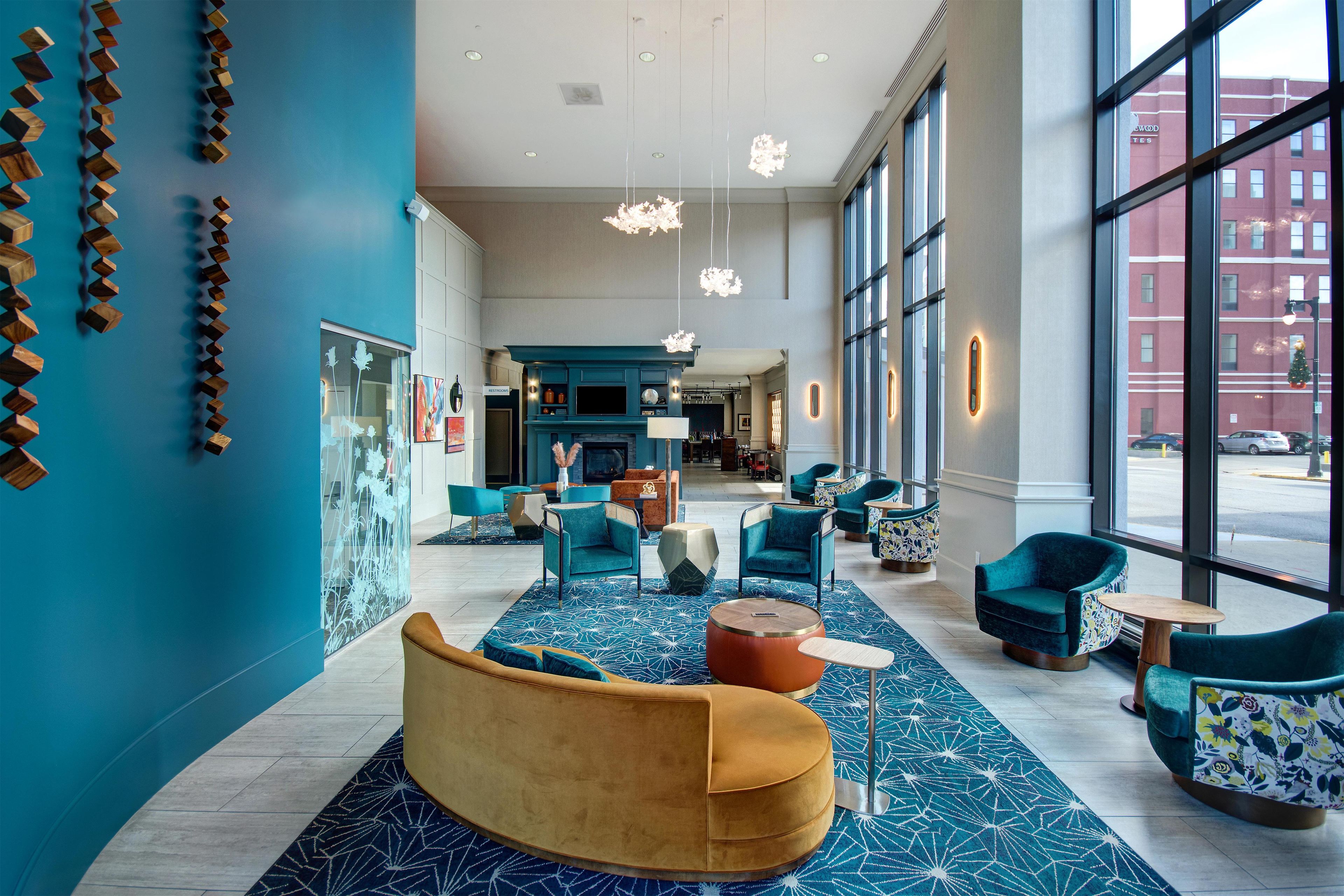 A modern lobby with seating areas, a fireplace, and large windows offering a view of the street.