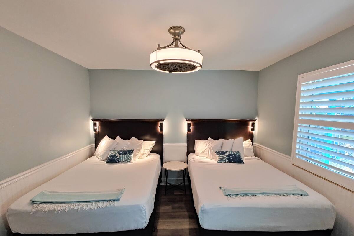 A hotel room with two beds, a small table, and a ceiling fan.