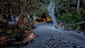 Een tuin 's nachts, met een hangmat, verlichte planten en een zandpad.