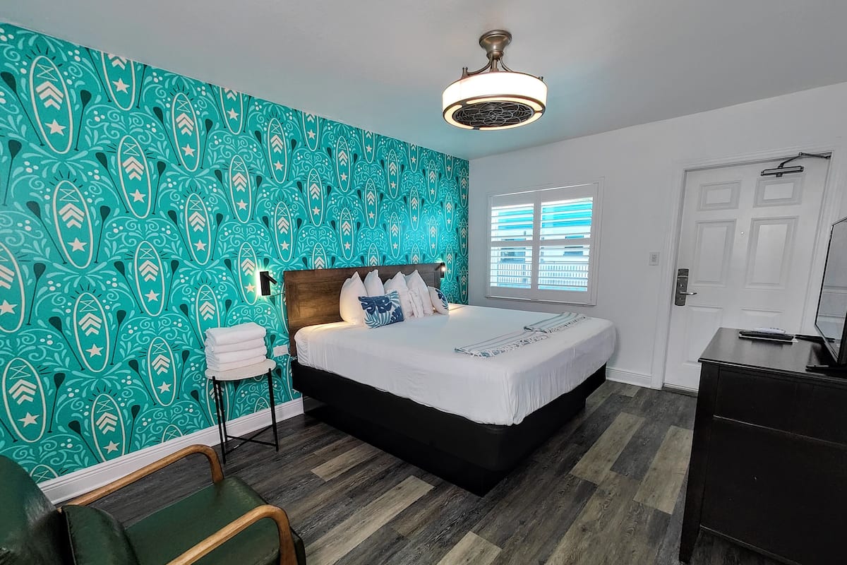 A bedroom with a bed, a nightstand, a chair, a dresser, and a window with blinds.