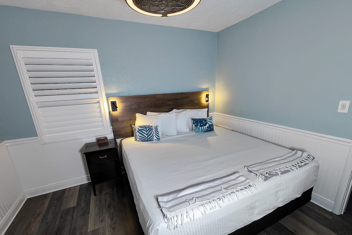 A bedroom with a large bed, a nightstand, a wall-mounted light, and a window with blinds.