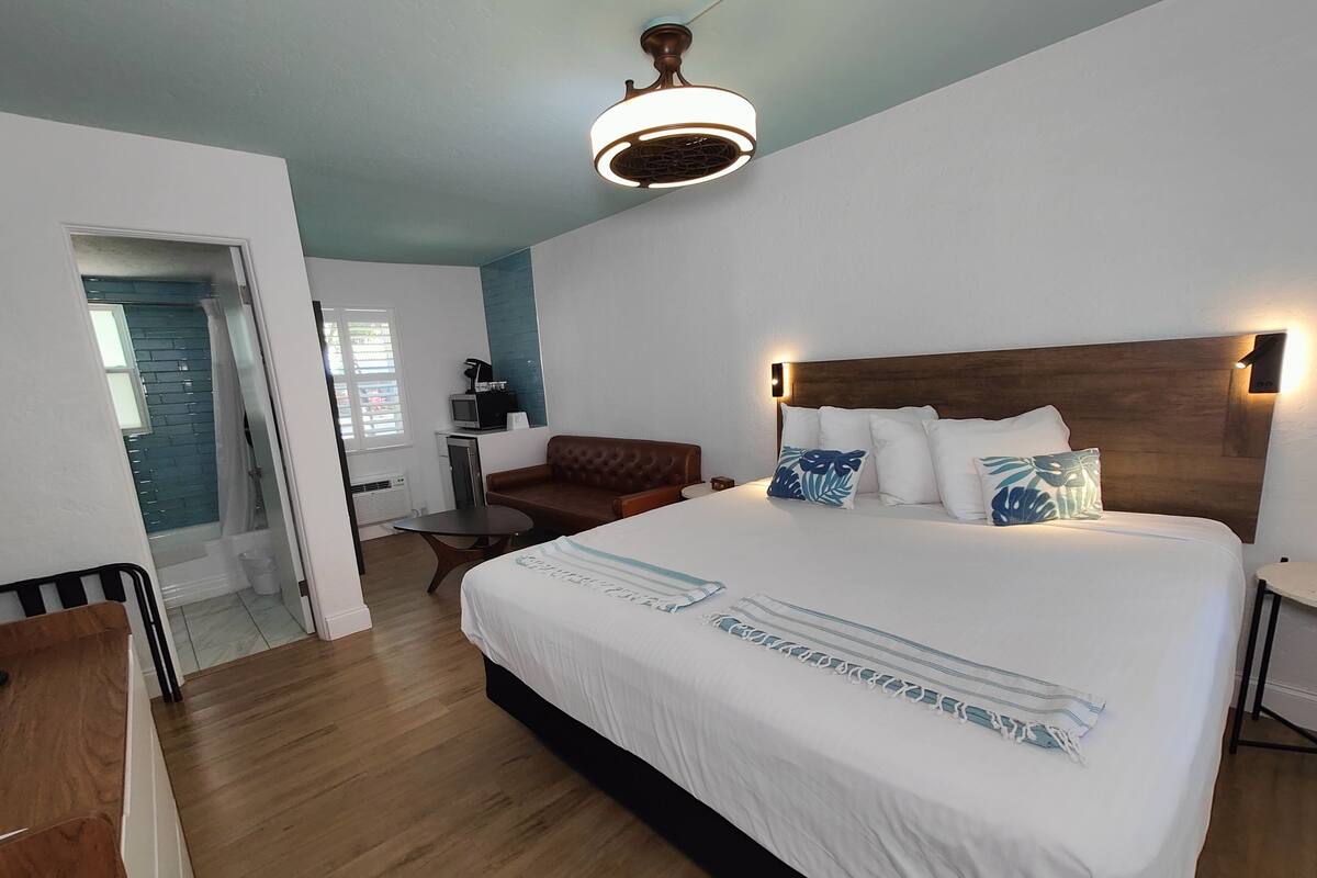 A bedroom with a large bed, a wooden headboard, a small table, a brown leather sofa, and a ceiling light fixture.