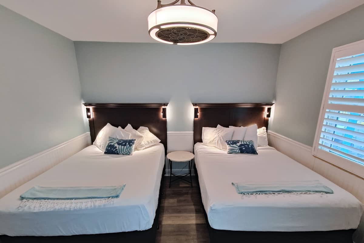 A hotel room with two single beds, a small round table, and a ceiling light fixture.