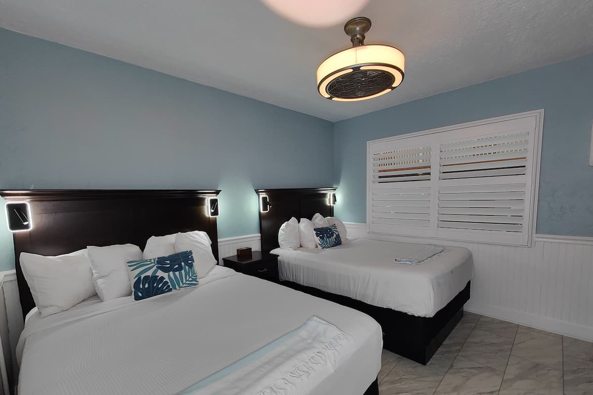 A hotel room with two beds, a ceiling fan, and a window with blinds.
