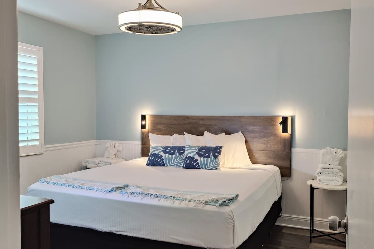 A bedroom with a bed, a wooden headboard, a ceiling fan, and a small table with towels.