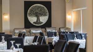 Un comedor con mesas dispuestas para el servicio, un cuadro grande de un árbol en la pared y una lámpara moderna.