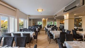 Ein Restaurant mit mehreren Tischen und Stühlen, großen Fenstern und einer Decke mit Einbuchtungslichtern.