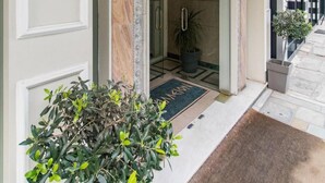 Entrada de hotel con puerta de cristal, lámpara decorativa en la pared y una planta en maceta.