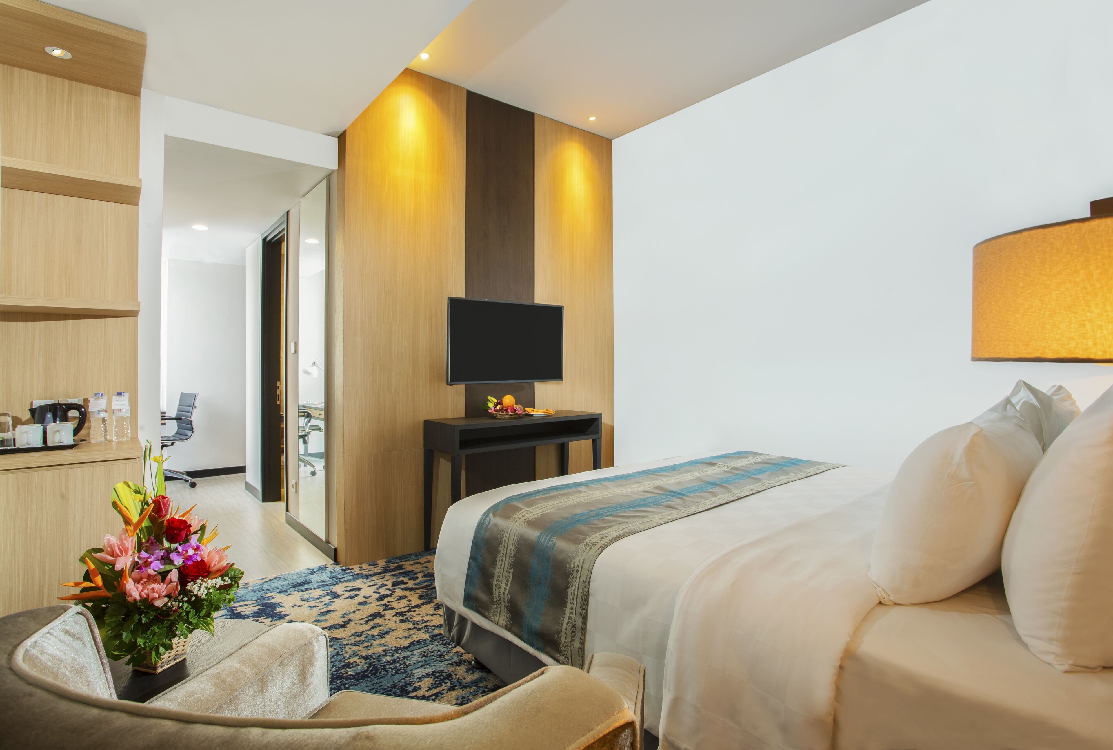 Una habitación de hotel con cama, escritorio, televisión y un arreglo floral.