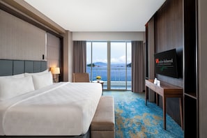 A hotel room with a large bed, a TV, a desk, and a view of the sea. - Swiss-Belhotel Papua (Jayapura)