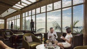 A modern lounge area with large windows, comfortable seating, and a table with tea and snacks. - Swiss-Belhotel Papua (Jayapura)