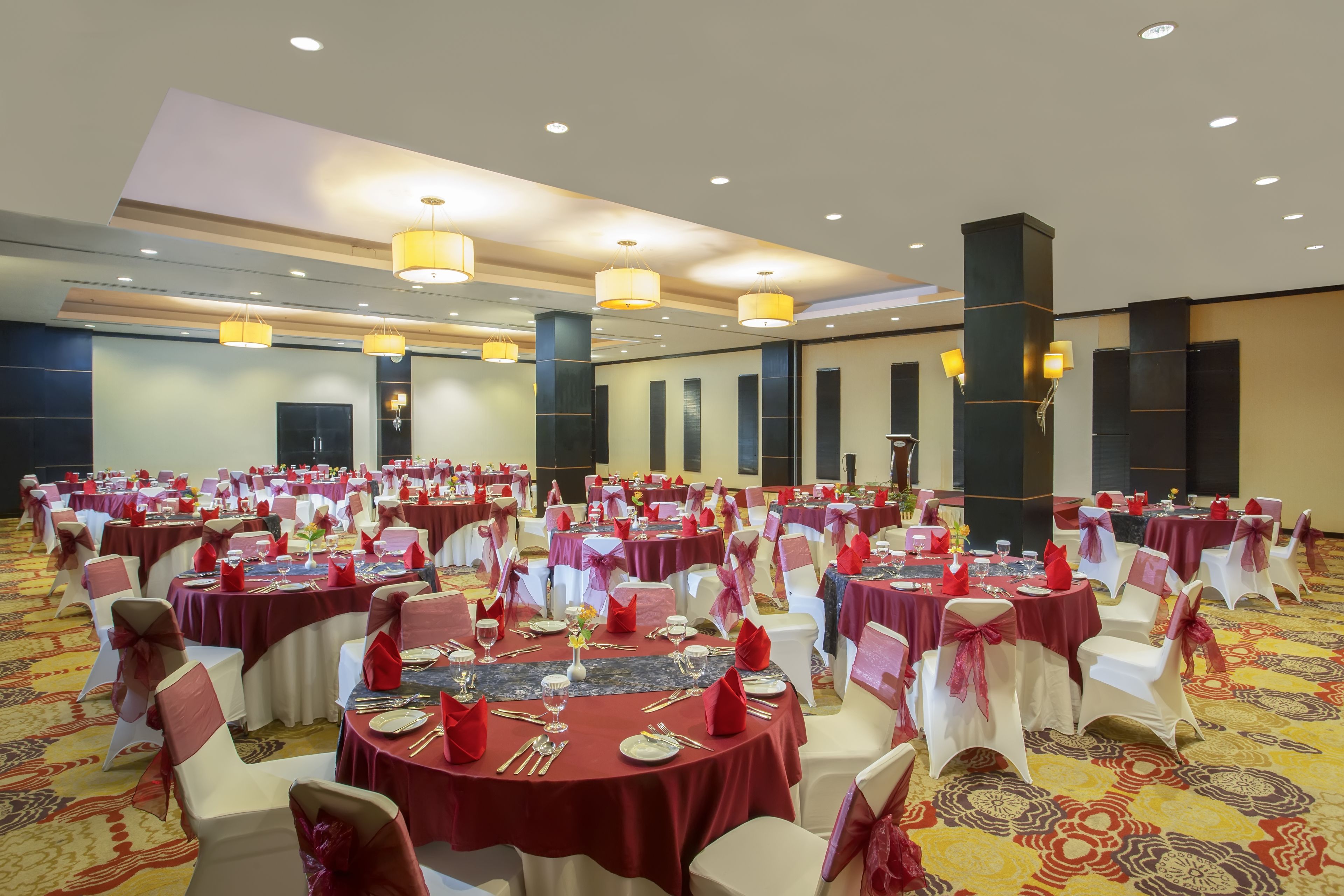 A banquet hall with round tables, white chairs, and red tablecloths.