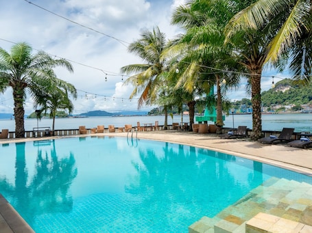 Une piscine bordée de chaises longues, de palmiers et offrant une vue sur la mer.. Swiss-Belhotel Papua