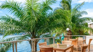 A balcony with wicker furniture overlooking a body of water, surrounded by palm trees. - Swiss-Belhotel Papua (Jayapura)