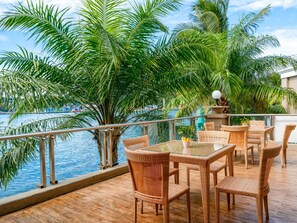 A balcony with wicker furniture overlooking a body of water, surrounded by palm trees. - Swiss-Belhotel Papua (Jayapura)