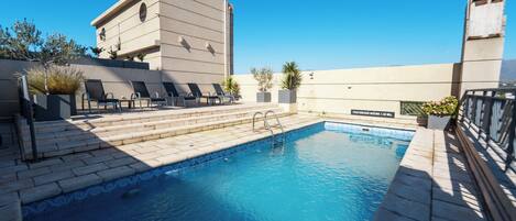 Una piscina con sillas de descanso y un edificio al fondo.