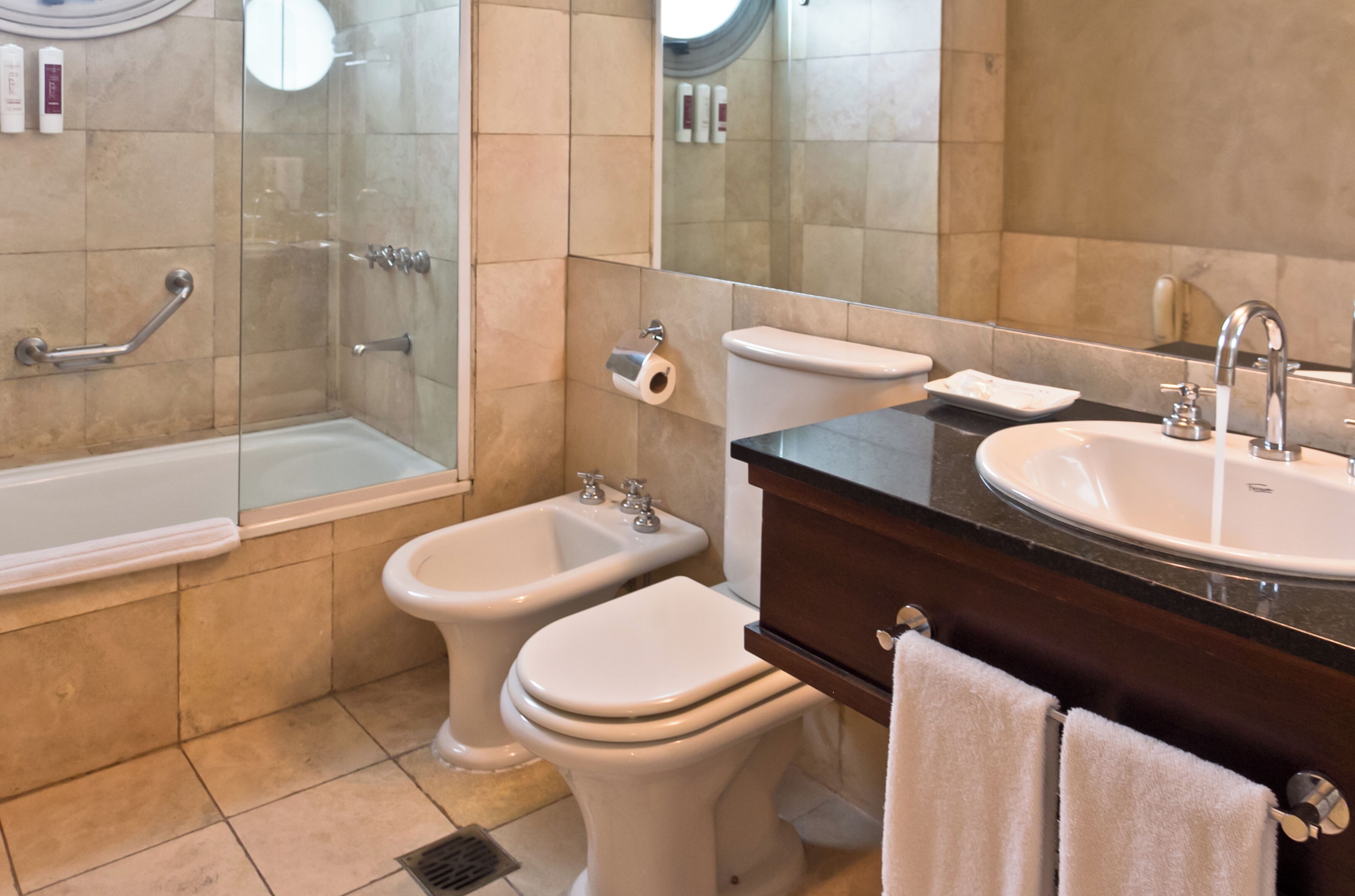A bathroom with a bathtub, two toilets, a bidet, a sink, and a mirror.