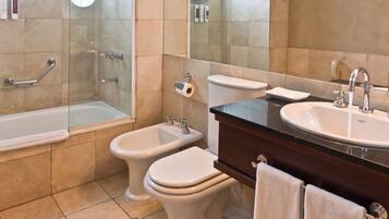 Een badkamer met een bad, twee toiletten, een bidet, een wastafel en een spiegel.