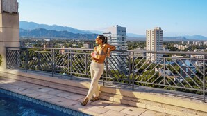 A person standing by a pool with a cityscape and mountains in the background.
