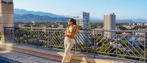 A person standing by a pool with a cityscape and mountains in the background.