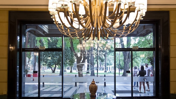 A lobby with a large chandelier, a glass door leading outside, and a small table with a decorative item.