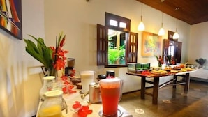 Un bufé de desayuno con diversos alimentos y bebidas, una máquina de café y un arreglo floral decorativo.