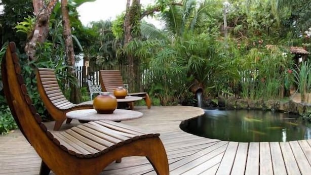 Una terraza de madera con sillones de descanso y un pequeño estanque.