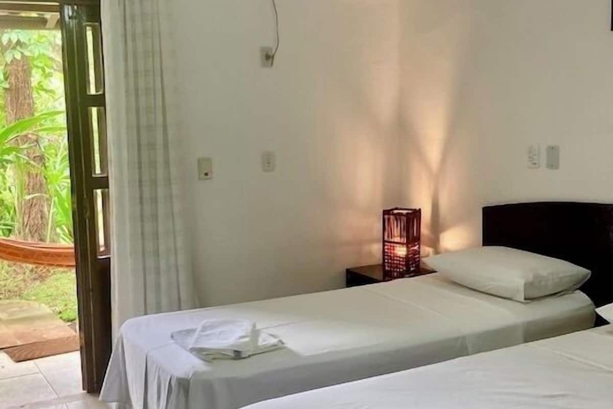 A room with two beds, an air conditioning unit, a ceiling fan, and a window with curtains.