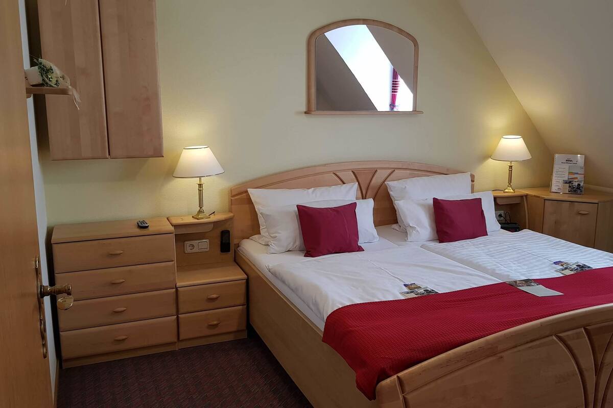 Une chambre à coucher bien rangée, avec un lit, deux tables de chevet dotées de lampes, une commode en bois et un miroir au mur.