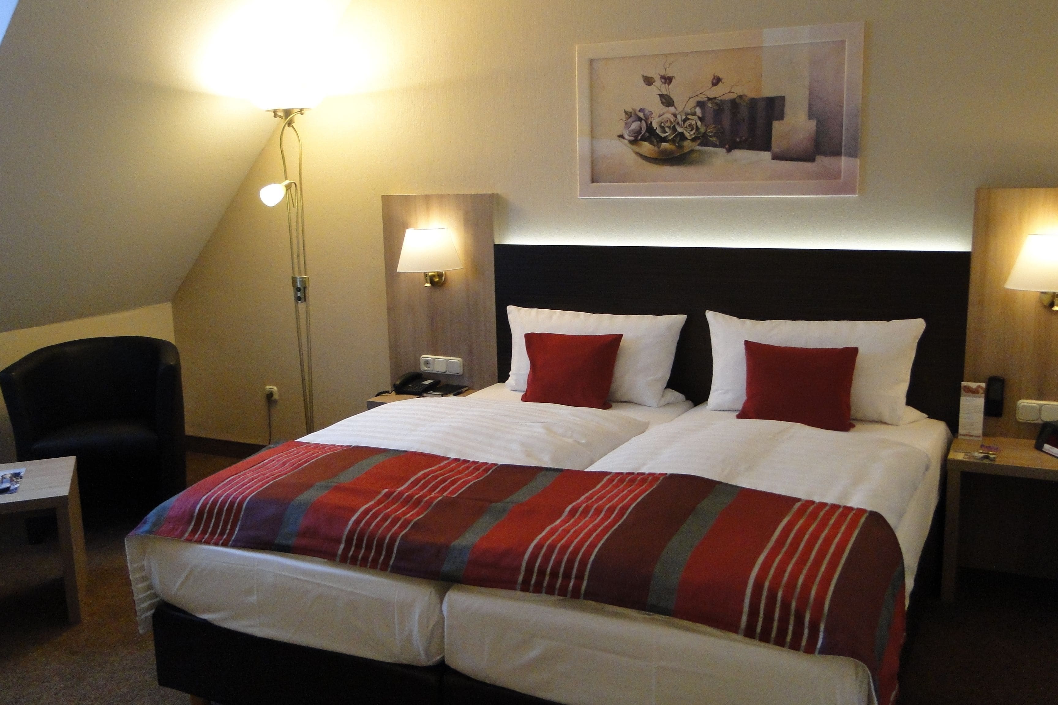Ein Hotelzimmer mit einem großen Bett, zwei Nachttischen, einem Sessel und einem Schreibtisch.