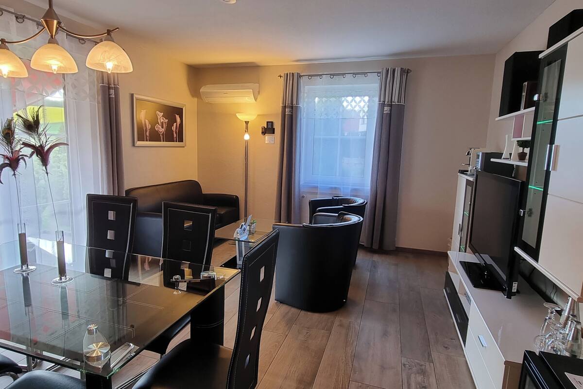 Un salon moderne avec une table à manger en verre, des chaises noires, un canapé et un téléviseur.