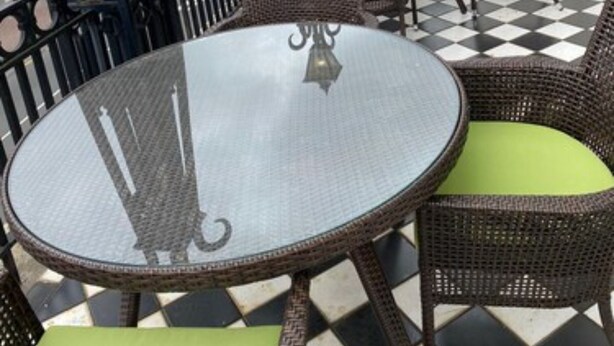 A rooftop terrace with round tables and wicker chairs, featuring a checkered floor pattern and decorative street lamps.