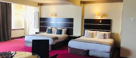 A hotel room with two beds, a dining table, and a chair.