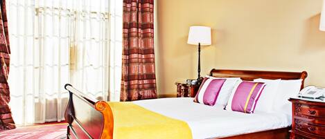 A hotel room with a wooden bed, a bedside table, a lamp, and a window with curtains.