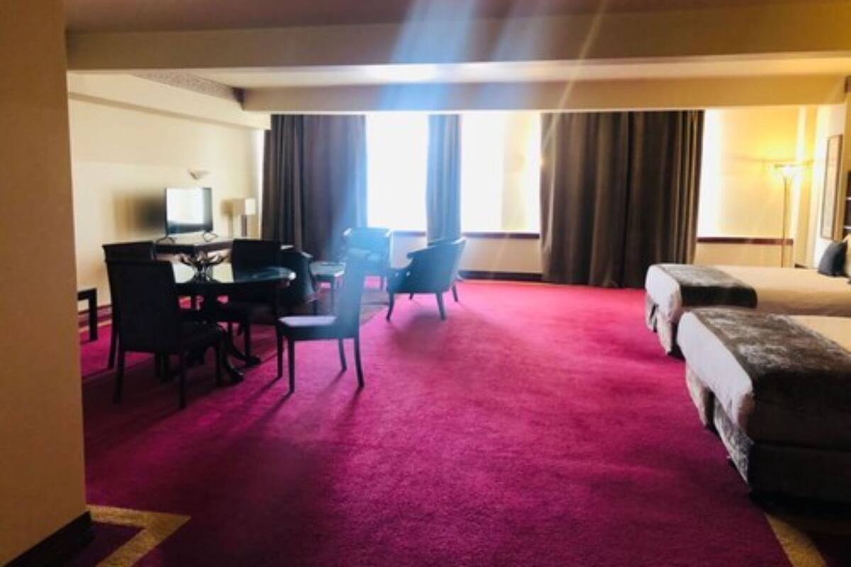 A hotel room with a red carpet, a bed, a desk with a chair, a television, and a window with curtains.