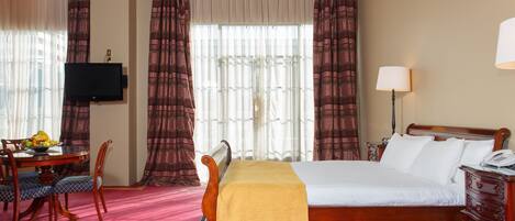 Una habitación de hotel con cama, escritorio, silla, televisor y lámpara.