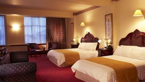 A hotel room with two beds, a sitting area with a chair, and a large window with curtains.