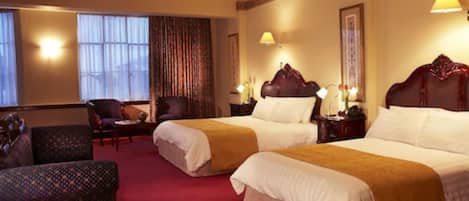 A hotel room with two beds, a sitting area with a chair, and a large window with curtains.
