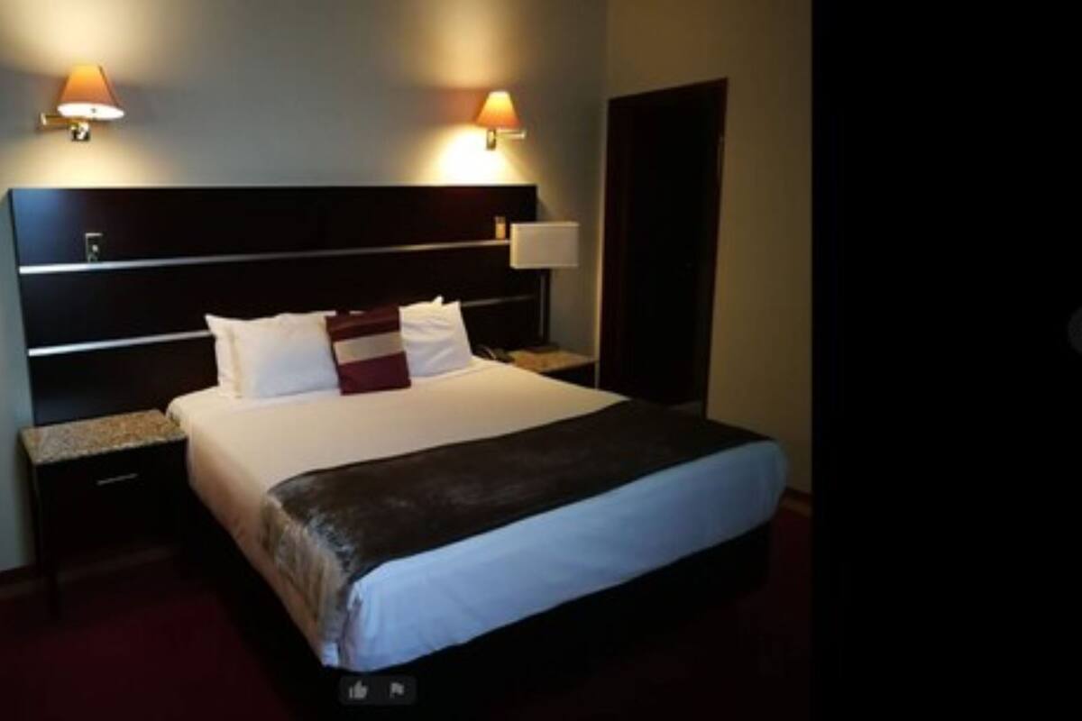 A hotel room with a large bed, two bedside tables, and two wall-mounted lamps.