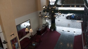 A hotel lobby with a chandelier, seating area, reception desk, and a large window overlooking the street.