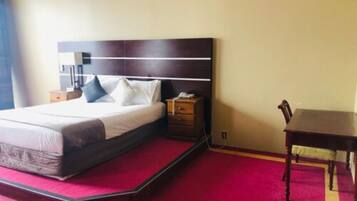 Una habitación de hotel con una cama, mesita de noche y una pequeña mesa de madera.